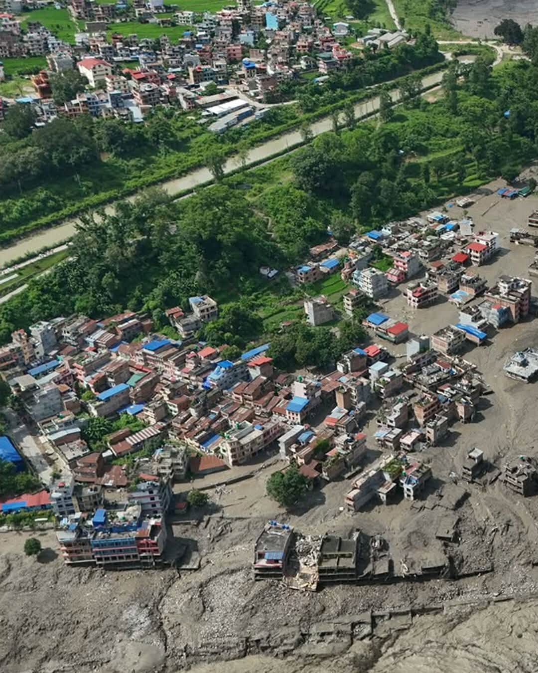 An aerial view of a Nepal village with rooftops surrounded by flood mud.