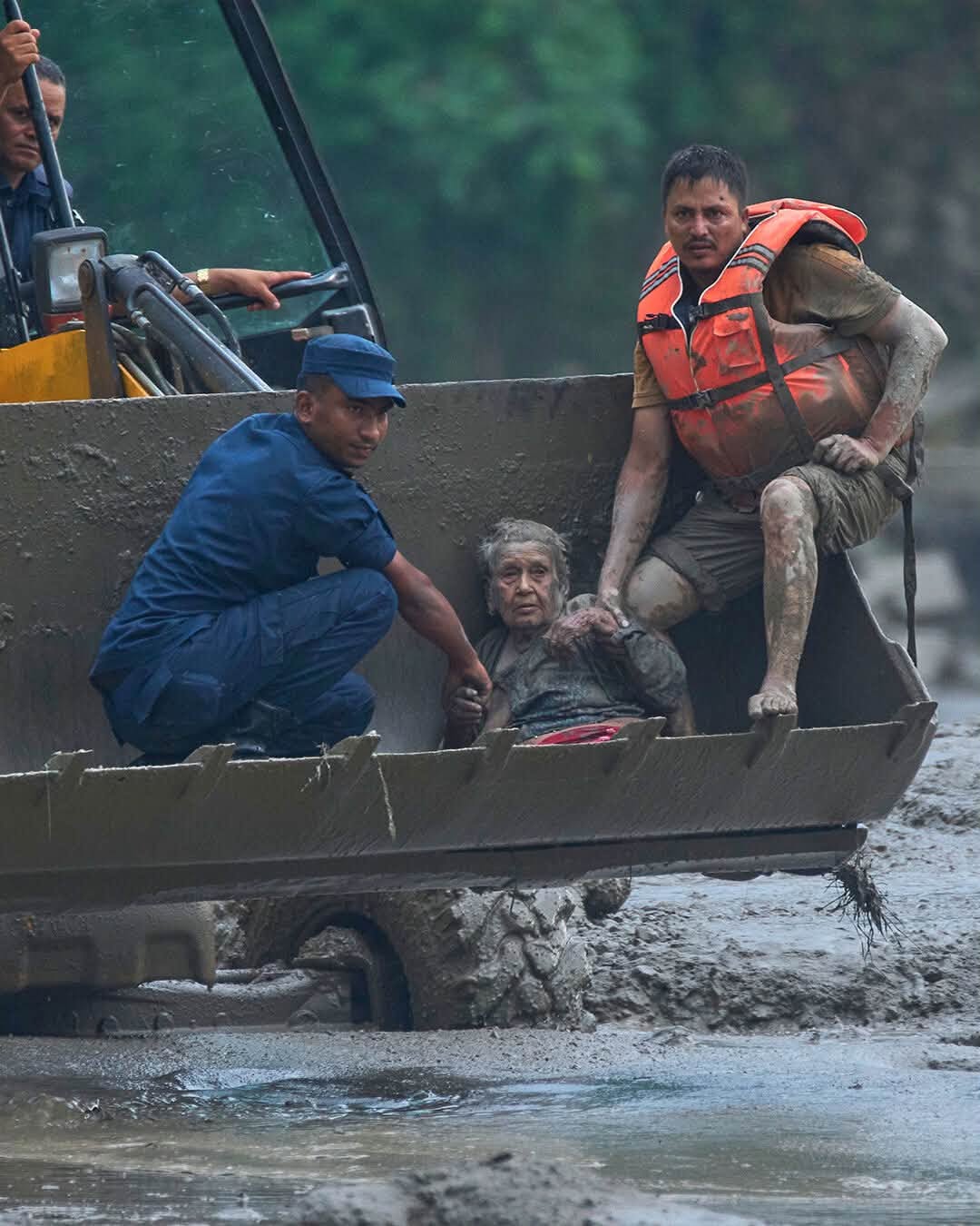 An elderly survivor is lifted to safety in the bucket of an excavator.