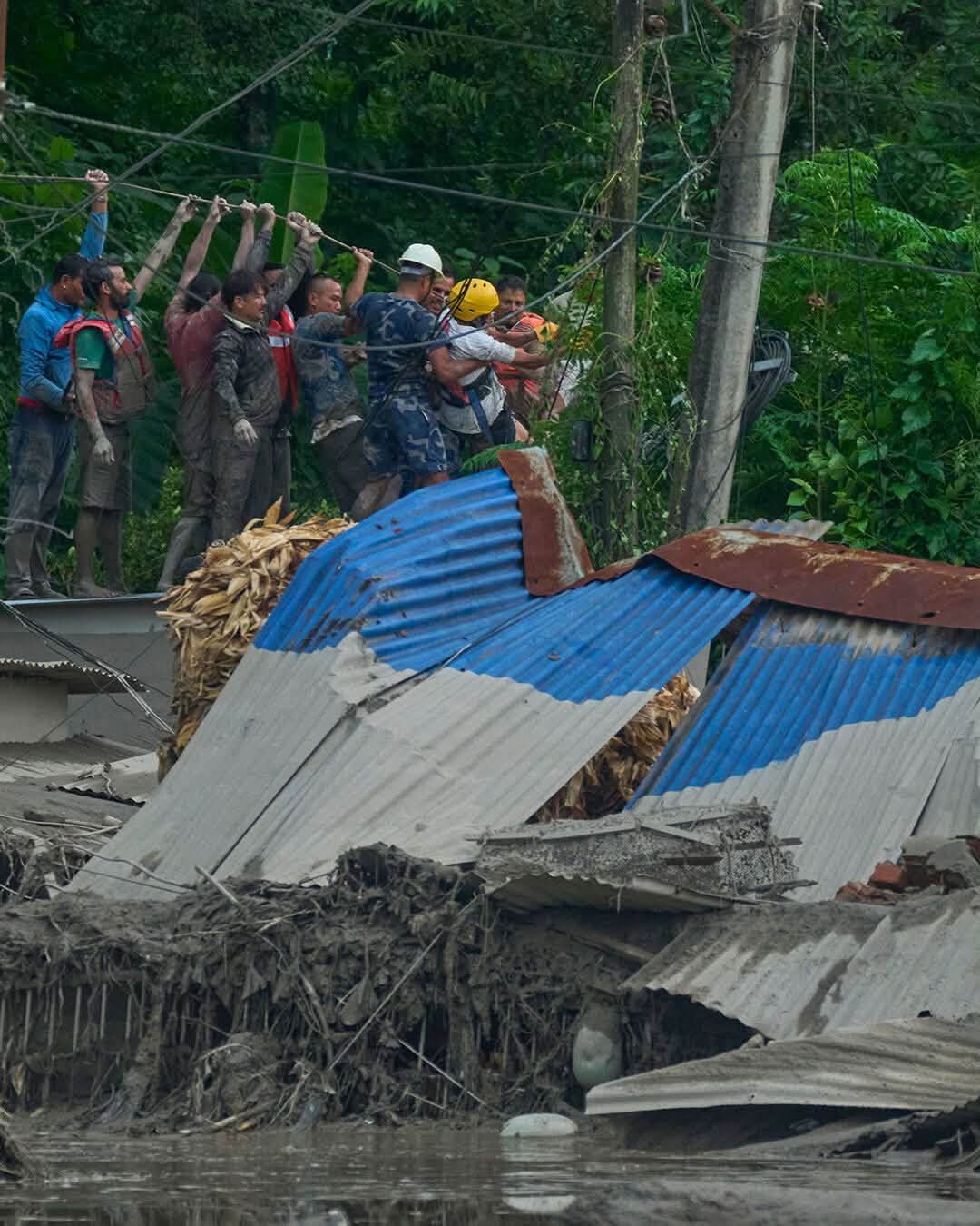 Rescue workers pull a survivor across a rope line over the debris.