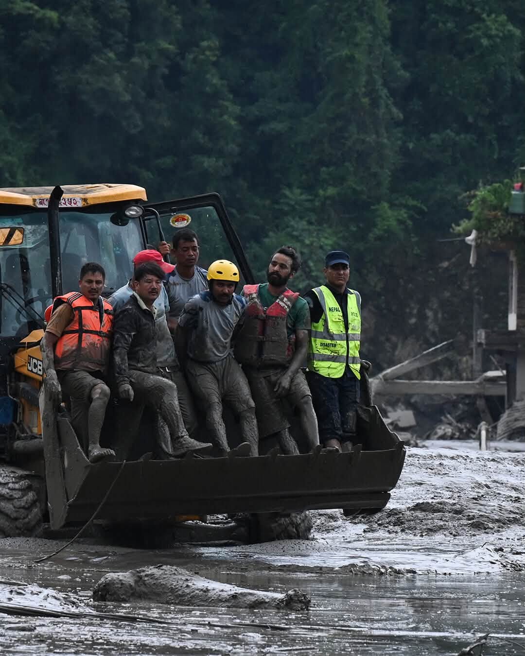 A group of mud-covered rescue workers and survivors in an excavator bucket.