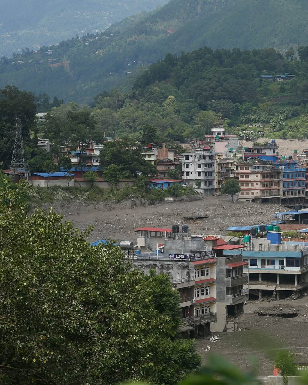 A hillside view overlooking a Nepal town beside a mud-filled riverbed.